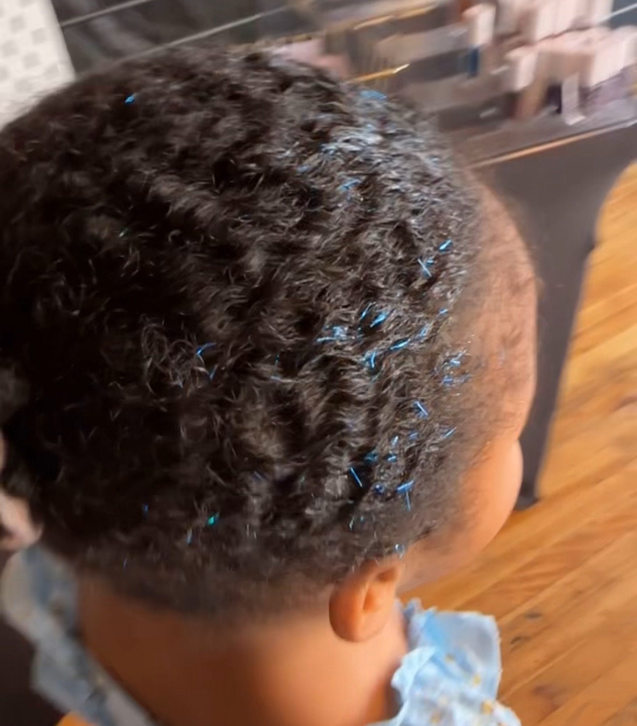 Arctic blue WildMane tinsel gel is applied to a slicked back ponytail on a 5 year old little girl with curly textured hair. It holds back her flyaways with medium hold and adds sparkle that matches her favorite tv show character, Bluey!