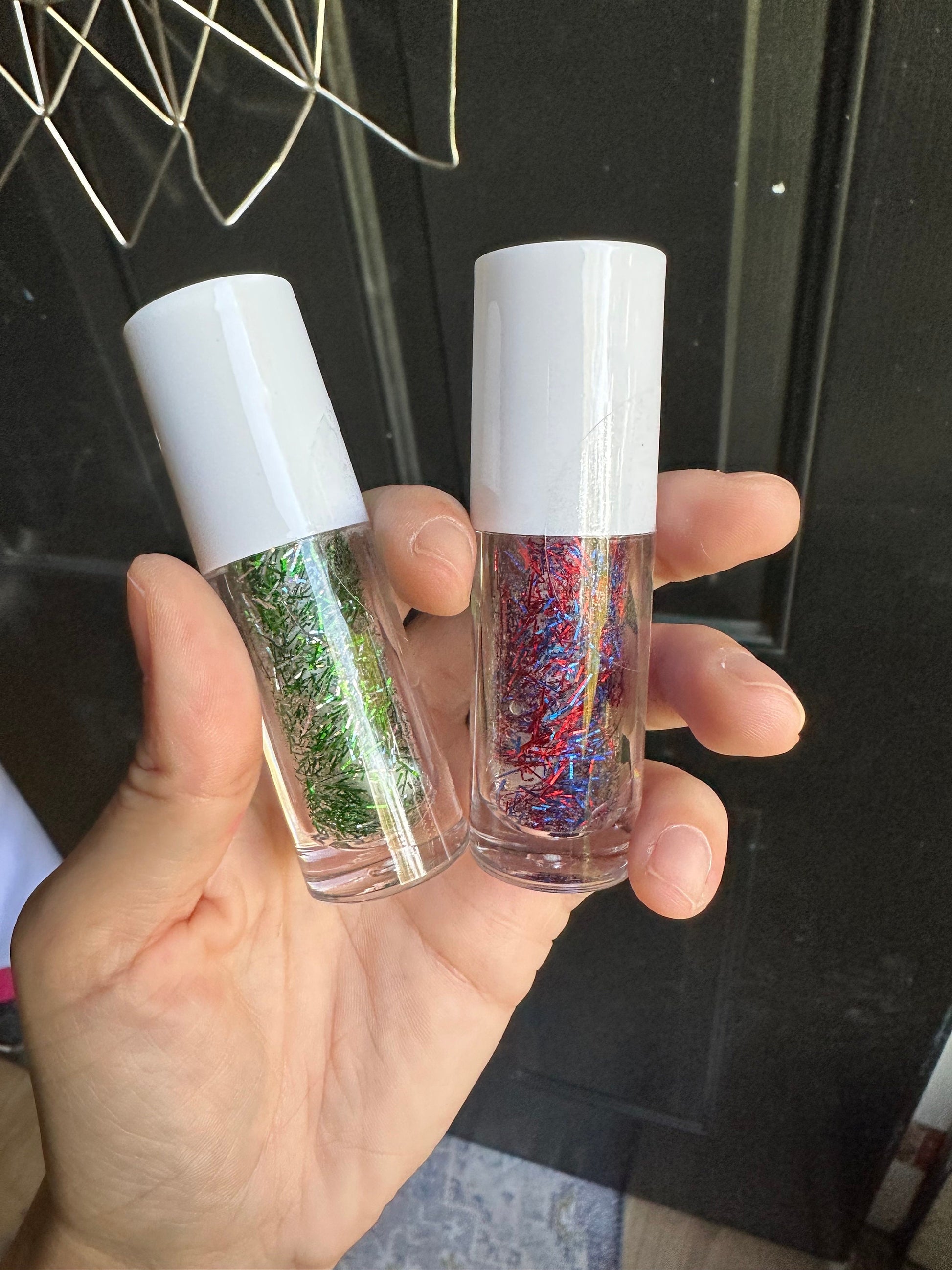 A hand holds two bottles of tinsel gel, on the left is a bottle with silver and green  to support her favorite football team, the Philadelphia Eagles.  The other is a mix of blue and red to support the Phillies and Memorial Day.